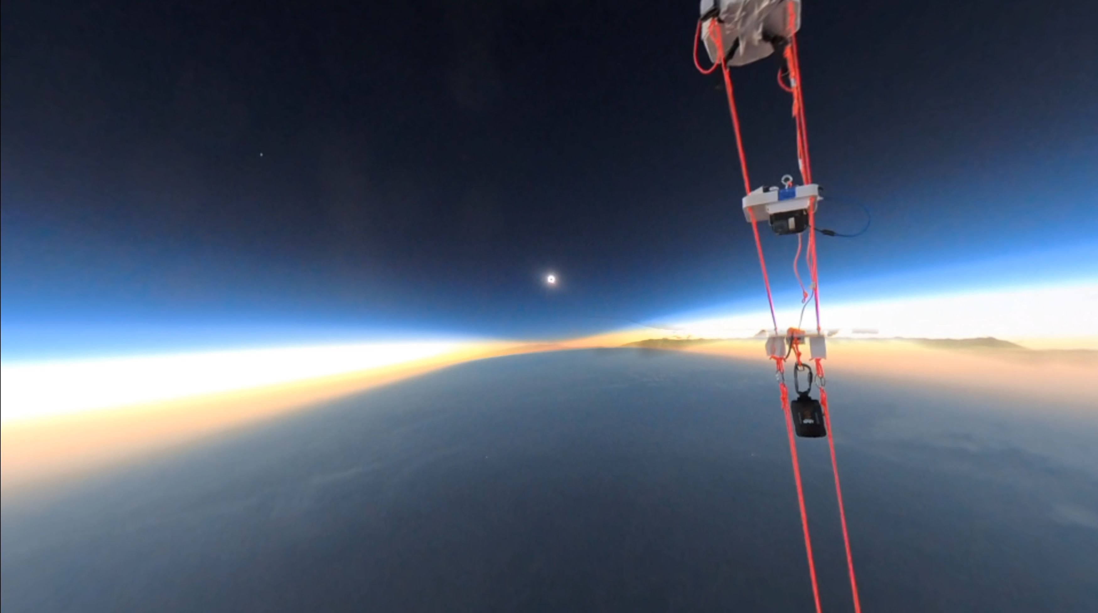 View of the Moon's shadow on Earth from a space-like perspective. Cameras and supporting payload lines in the foreground.