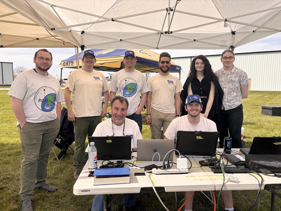 A team of people behind a table covered in laptops and technology running the ground station
