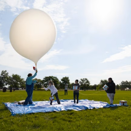 The sun streaming over a group of people releasing a balloon