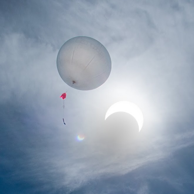 A balloon in the sky next to an eclipsed sun