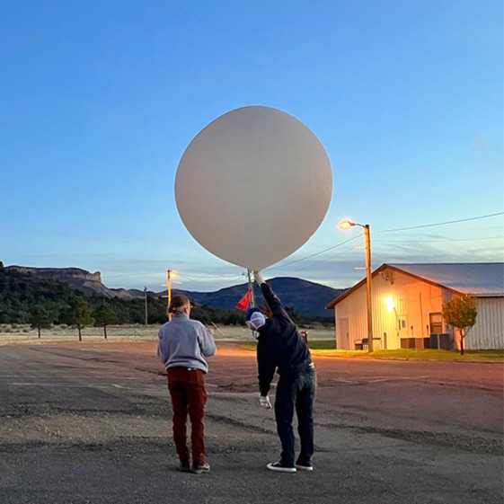 Two people holding a balloon in a parking lot at sunrise
