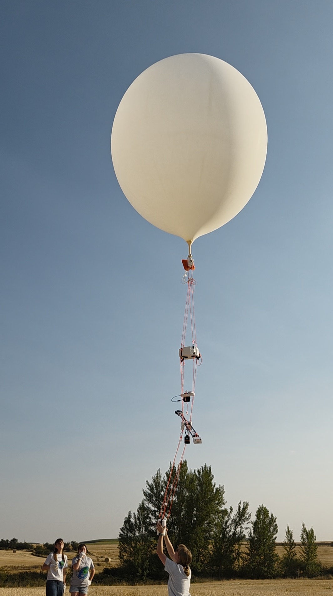 Large weather balloon with payloads hanging beneath and a female student about to release it.